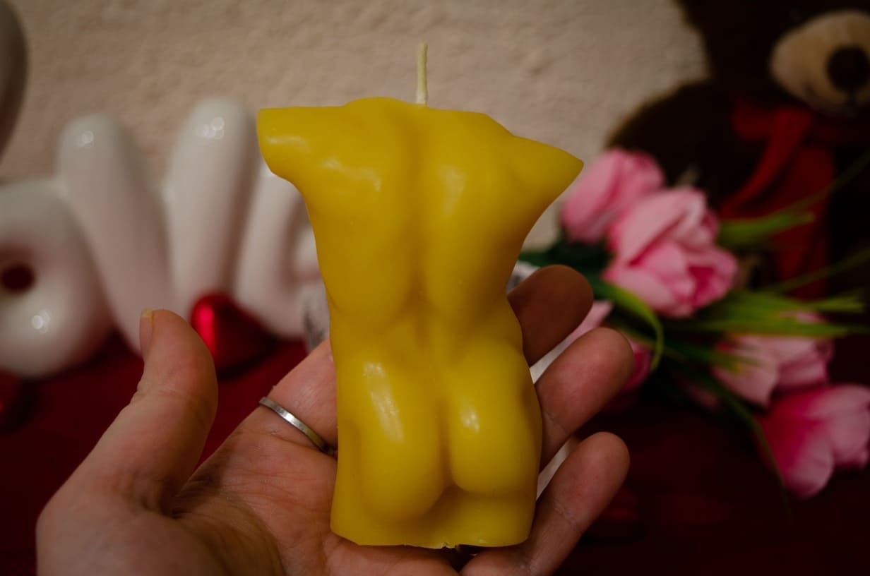 Rankoje laikoma natūralaus bičių vaško vyro kūno formos žvakė iš nugaros.