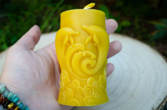 Cilindrinė žvakė su pavaizduotais delfinais laikoma rankoje