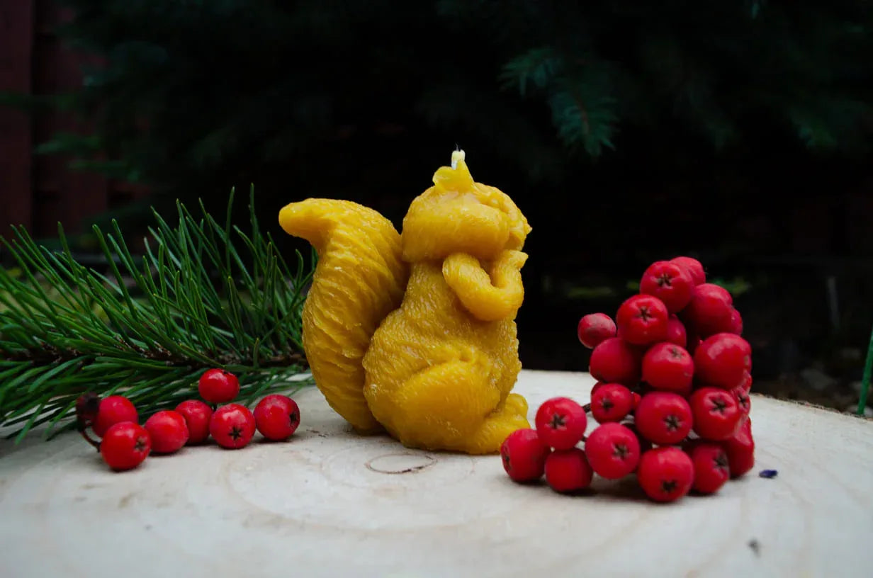 Natūralaus bičių vaško žvakė voverės formos pastatyta ant kelmo šonu.