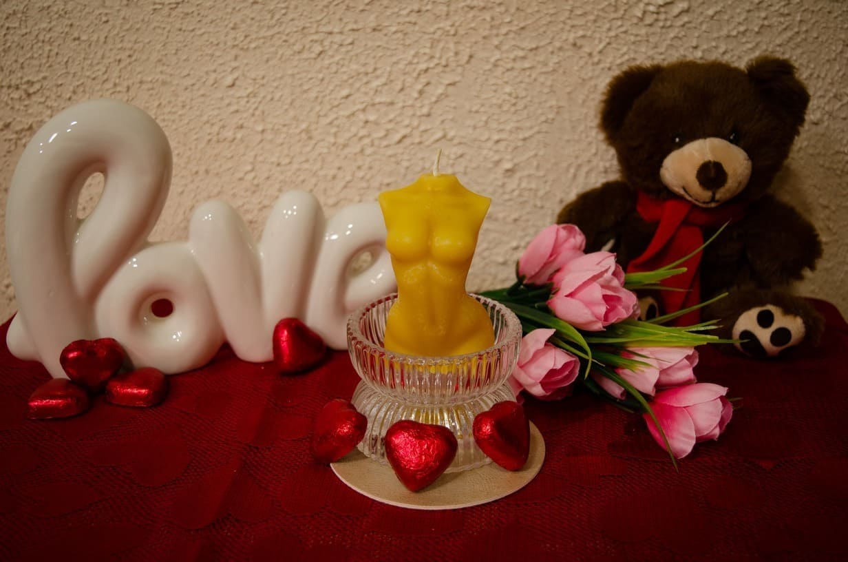 Natūralaus bičių vaško moters kūno formos žvakė pastatyta stiklinėje žvakidėje.