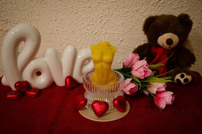 Natūralaus bičių vaško moters kūno formos žvakė pastatyta stiklinėje žvakidėje.