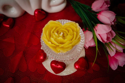 Priartinta iš viršaus geltona, širdies formos, rožės išvaizdos natūralaus bičių vaško žvakė.