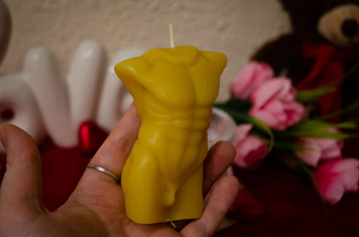 Rankoje laikoma natūralaus bičių vaško  vyro kūno formos žvakė iš priekio.