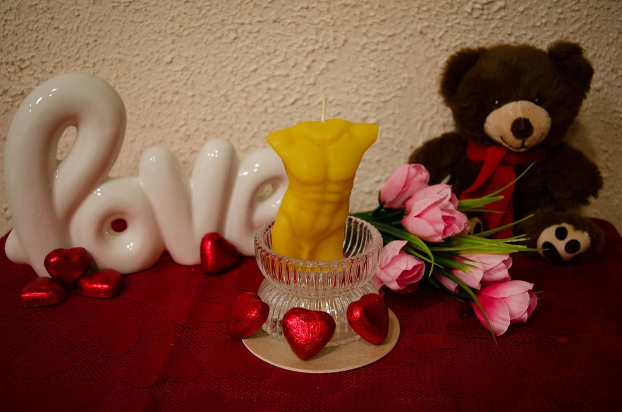 Natūralaus bičių vaško žvakė vyro kūno formos pastatyta romantiškoje kompozicijoje.