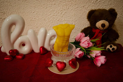 Natūralaus bičių vaško žvakė vyro kūno formos pastatyta romantiškoje kompozicijoje.