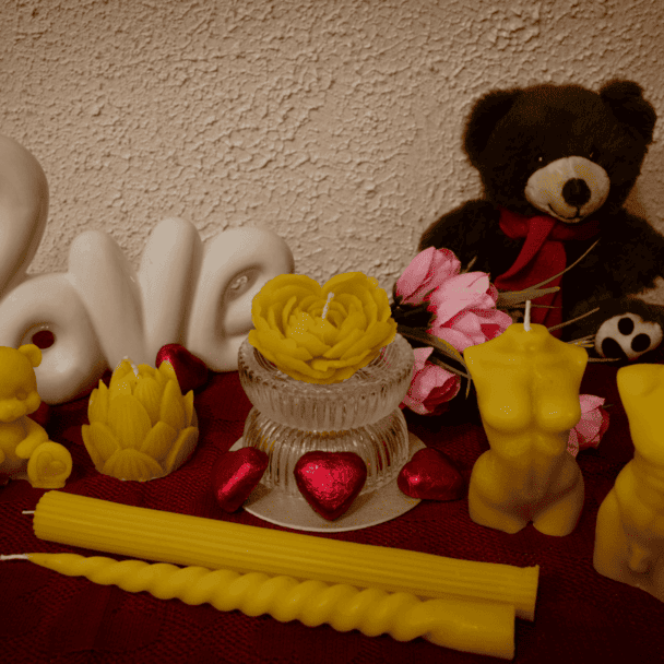 Geltonų bičių vaško žvakių rinkinys: širdis rože, moters kūno,vyro kūno, meškučio, lotoso ir suktų formų žvakės romantiškoje kompozicijoje su meškučiu bei dekoratyviniu užrašu „Love“.