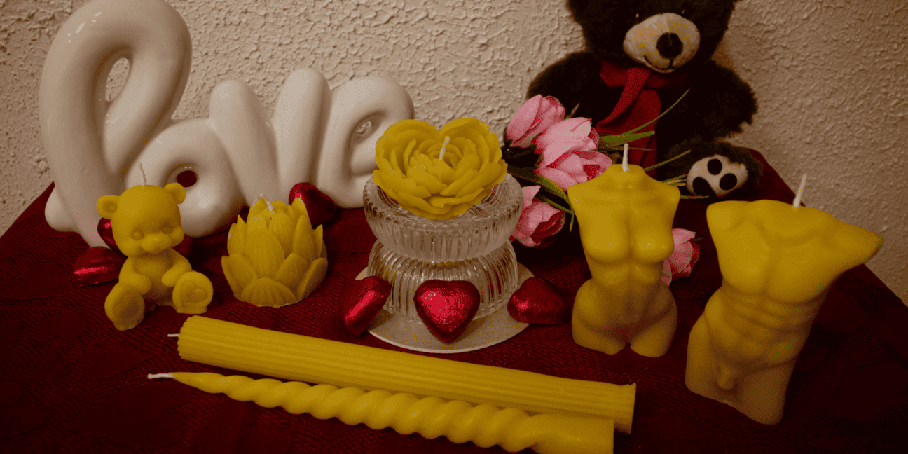 Geltonų bičių vaško žvakių rinkinys: širdies rožės, moters kūno,vyro kūno, meškučio  ir suktų formų žvakės romantiškoje kompozicijoje su meškučiu bei dekoratyviniu užrašu „Love“.