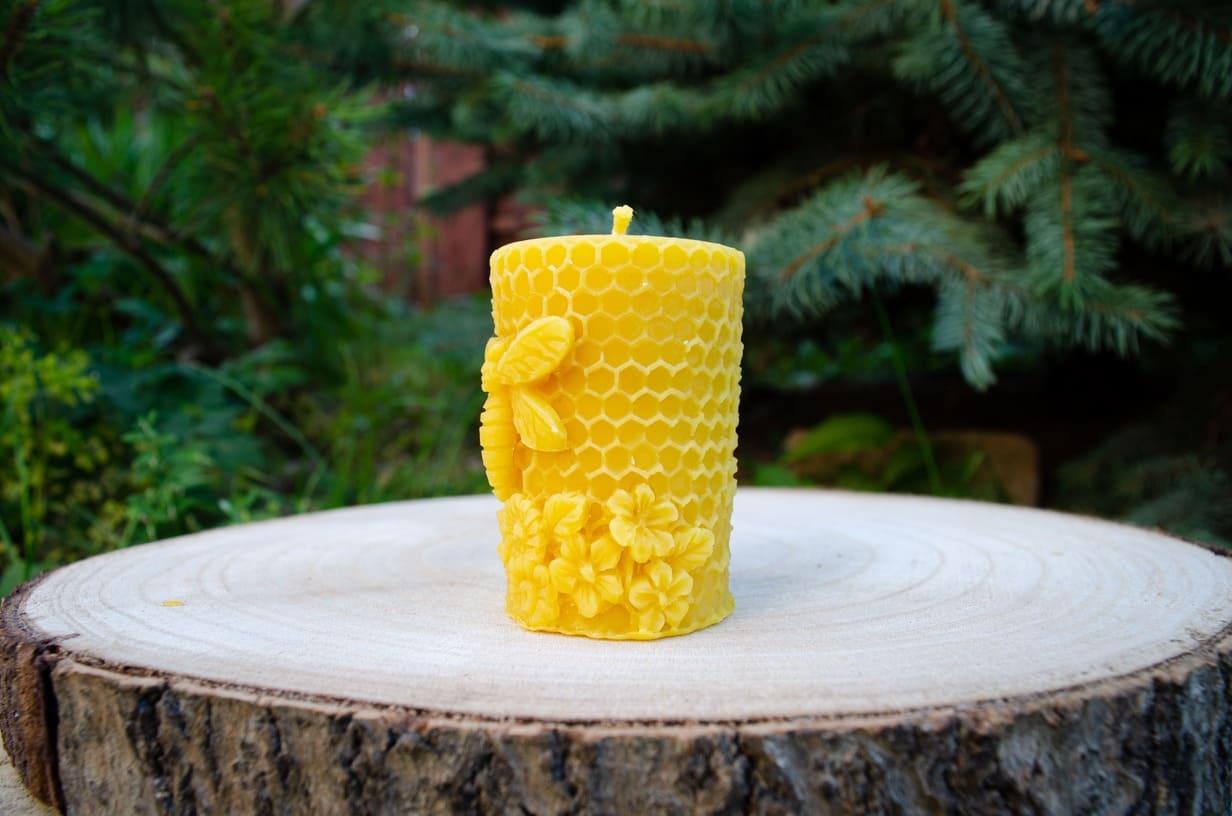 Geltona bičių vaško žvakė su korio raštu, bitute ir gėlėmis ant medinio pagrindo.