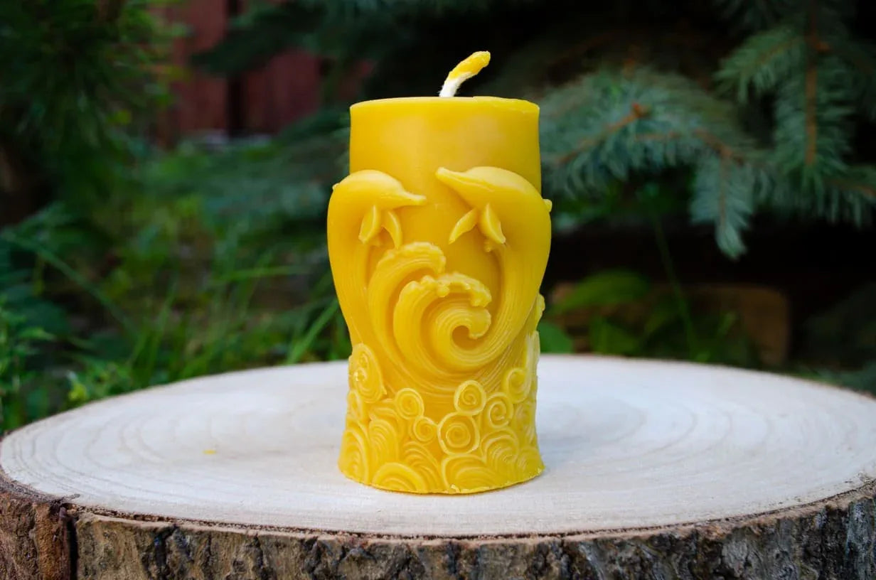 Cilindrinė žvakė su pavaizduotais delfinais pastatyta ant kelmo