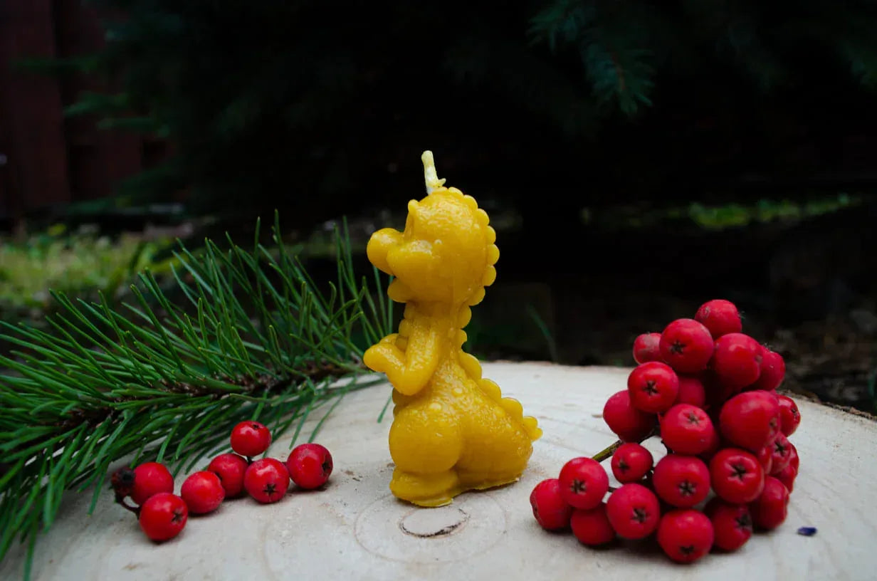 Melora natūralaus bičių vaško žvakė drakoniuko formos pastatyta ant kelmo šonu.