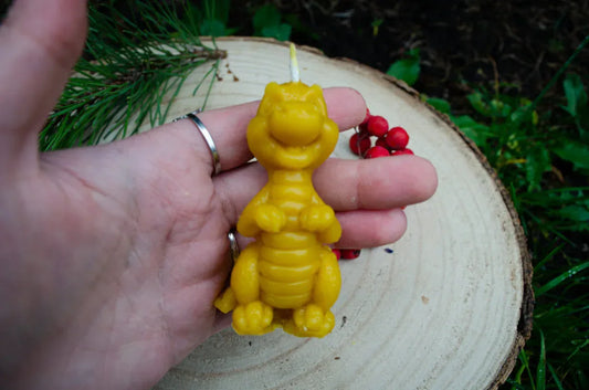 Rankoje laikoma natūralaus bičių vaško žvakė drakoniuko formos.