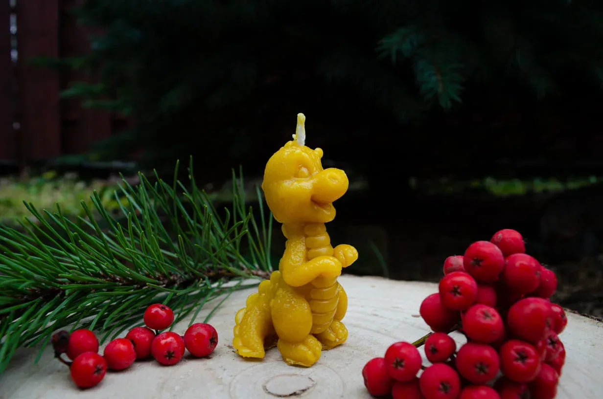 Natūralaus bičių vaško žvakė drakoniuko formos pastatyta ant kelmo šonu.