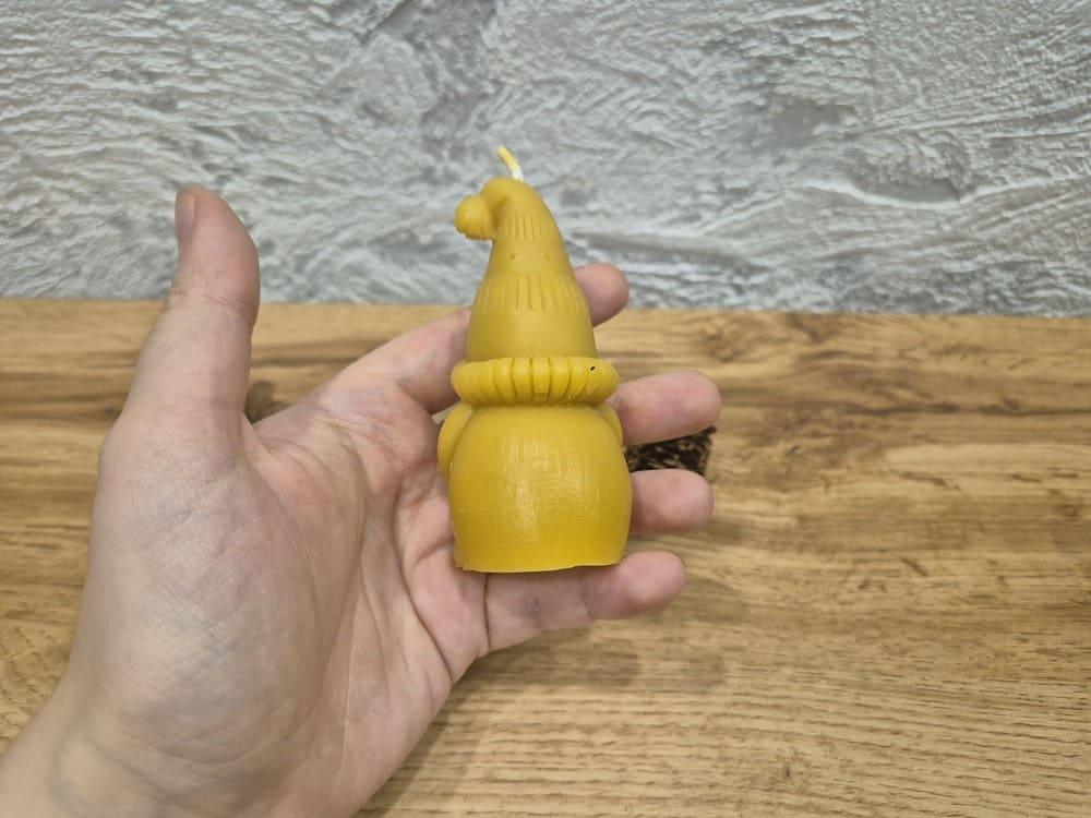 Bičių vaško žvakė "elfas su snaige" laikoma rankoje atsukus žvakės nugara į žiūrovą.