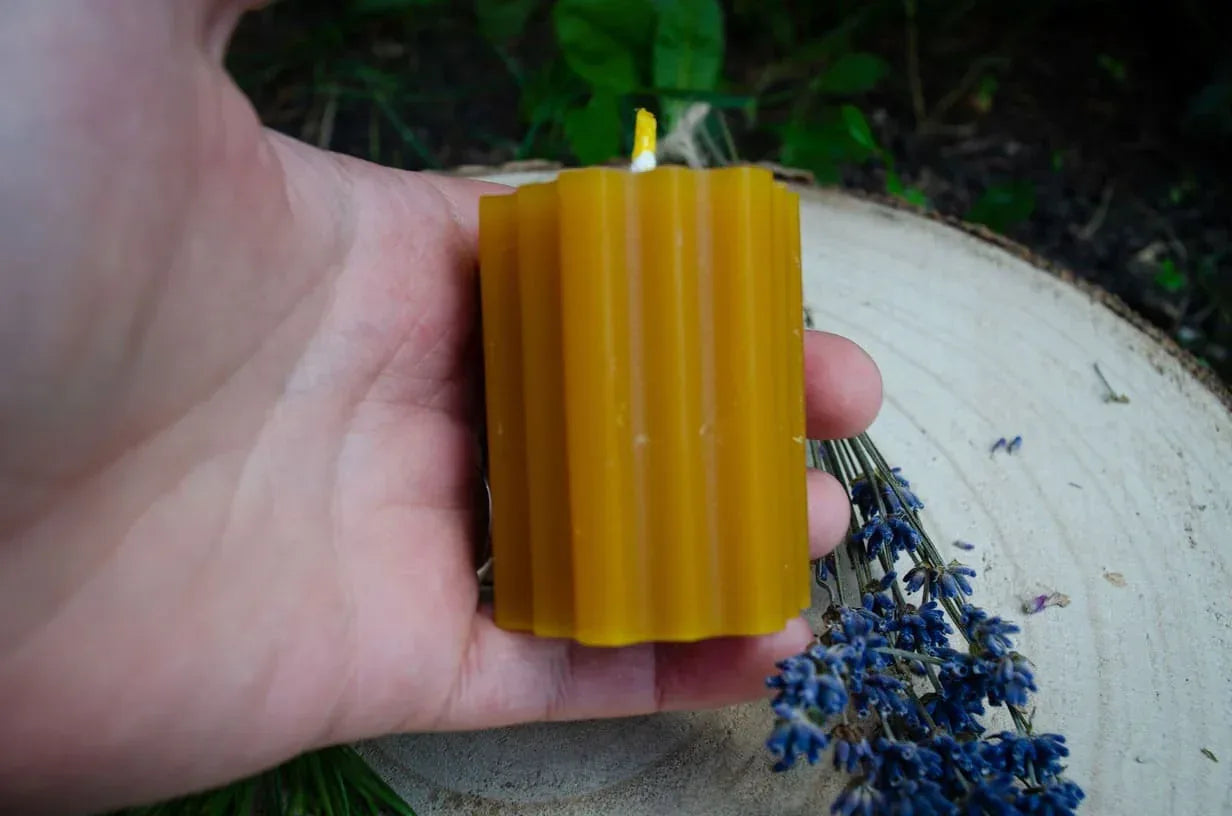 Natūralaus bičių vaško žvakė Hexas laikoma rankoje.