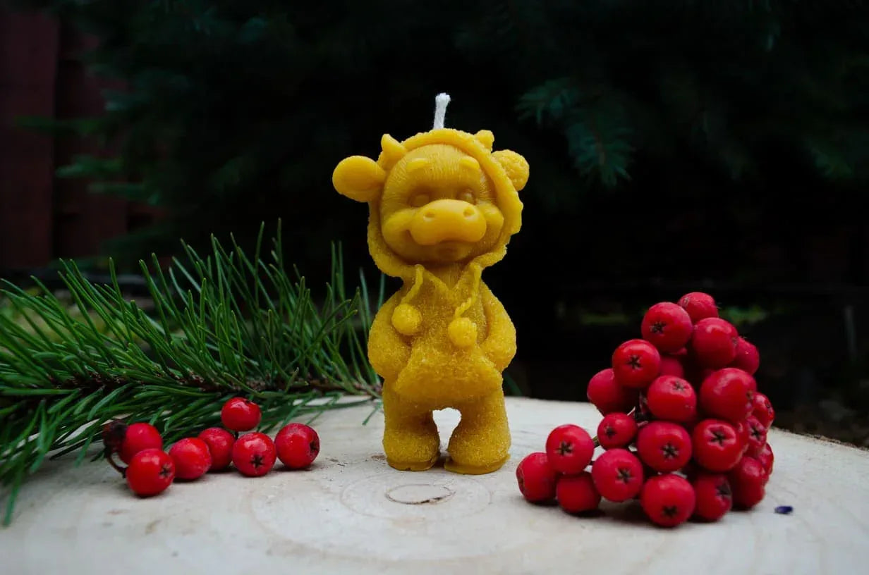 Natūralaus bičių vaško žvakė karvytė pastatyta ant kelmo.