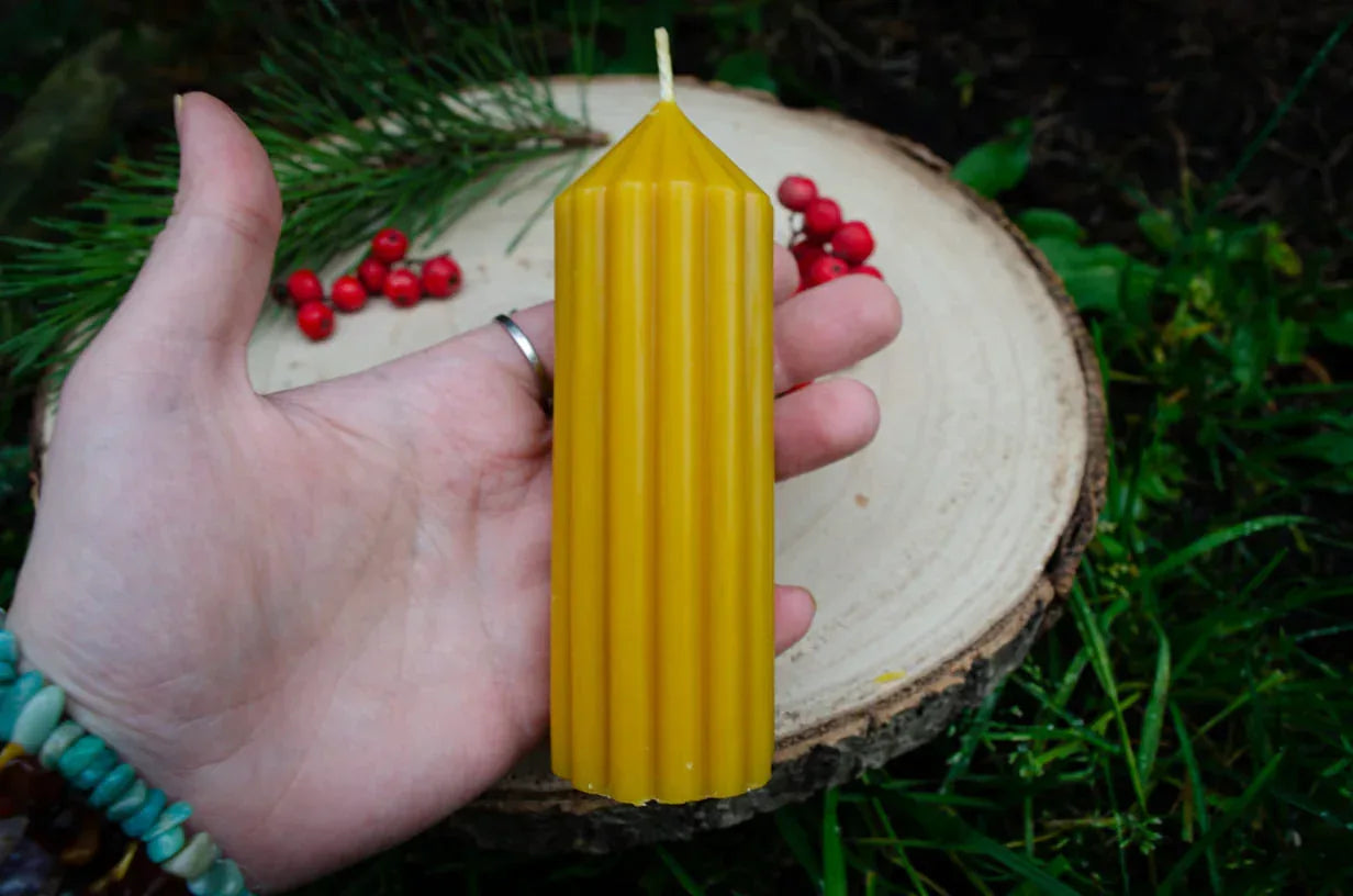 Rankoje laikoma natūralaus bičių vaško žvakė smailas cilindras demonstruojant jos dydį.
